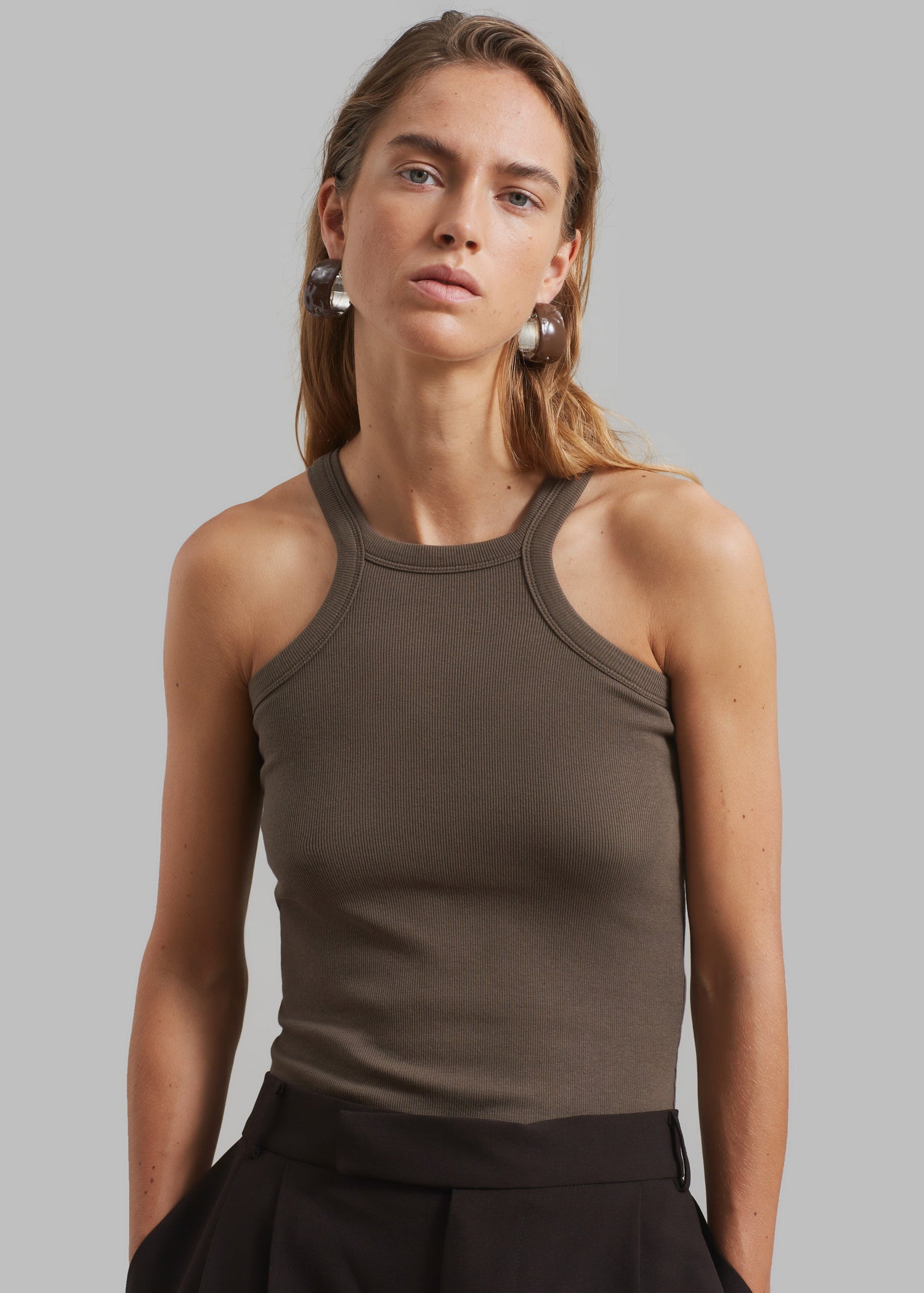 A woman wearing a brown halter tank top with a high round neckline and cut-out detail, paired with a black skirt.