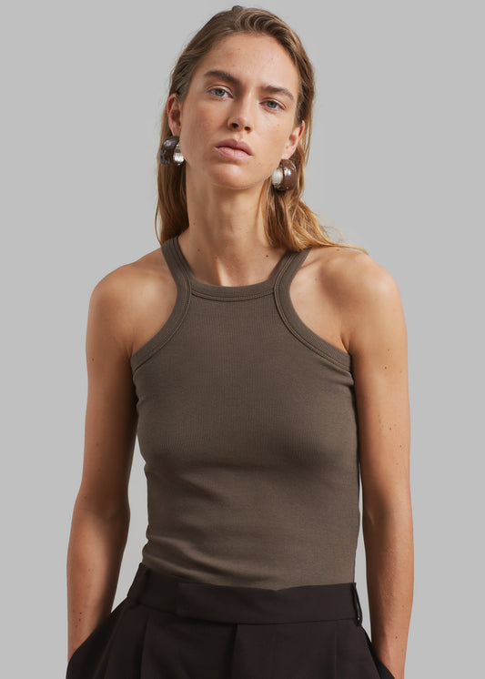 A woman wearing a brown halter tank top with a high round neckline and cut-out detail, paired with a black skirt.